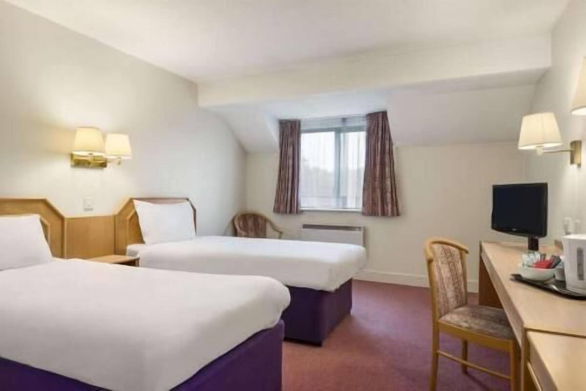 A hotel room with two beds, a desk with a chair, a television, and a window with curtains.