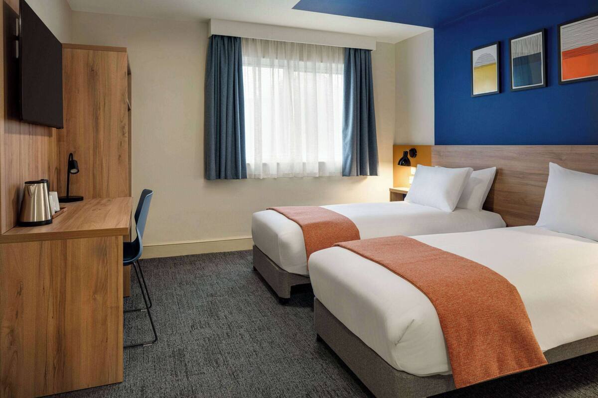 A hotel room with two beds, a desk, a chair, a TV, and a window with curtains.