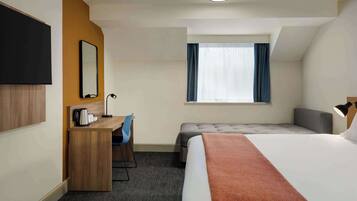 A hotel room with a bed, a desk, a chair, a TV, a window, and a ceiling light.
