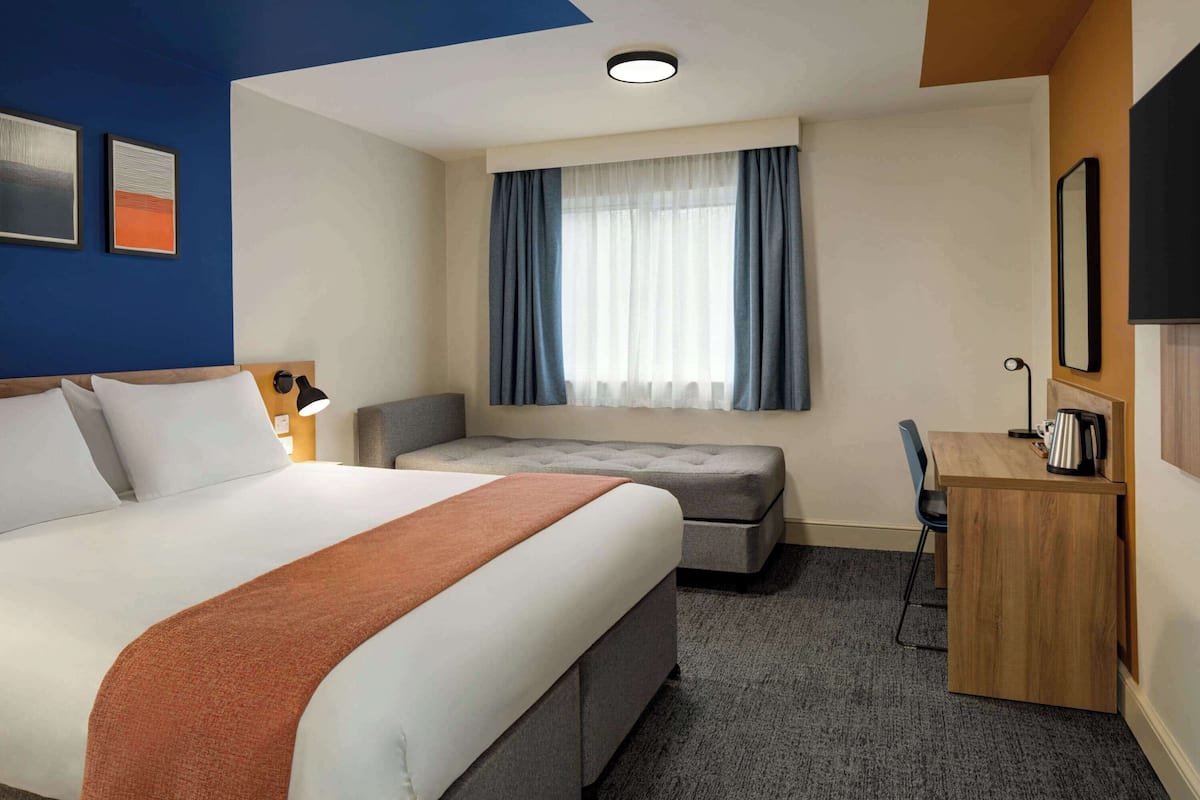 A hotel room with a large bed, a desk, a chair, a sofa, and a window with curtains.