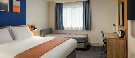 A hotel room with a large bed, a desk, a chair, a sofa, and a window with curtains.