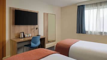 A hotel room with two beds, a desk with a chair, a flat-screen TV, a mirror, and a window with curtains.