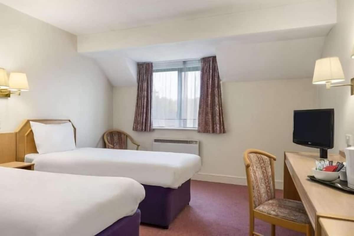 A hotel room with two beds, a desk, a chair, a television, and a window with curtains.