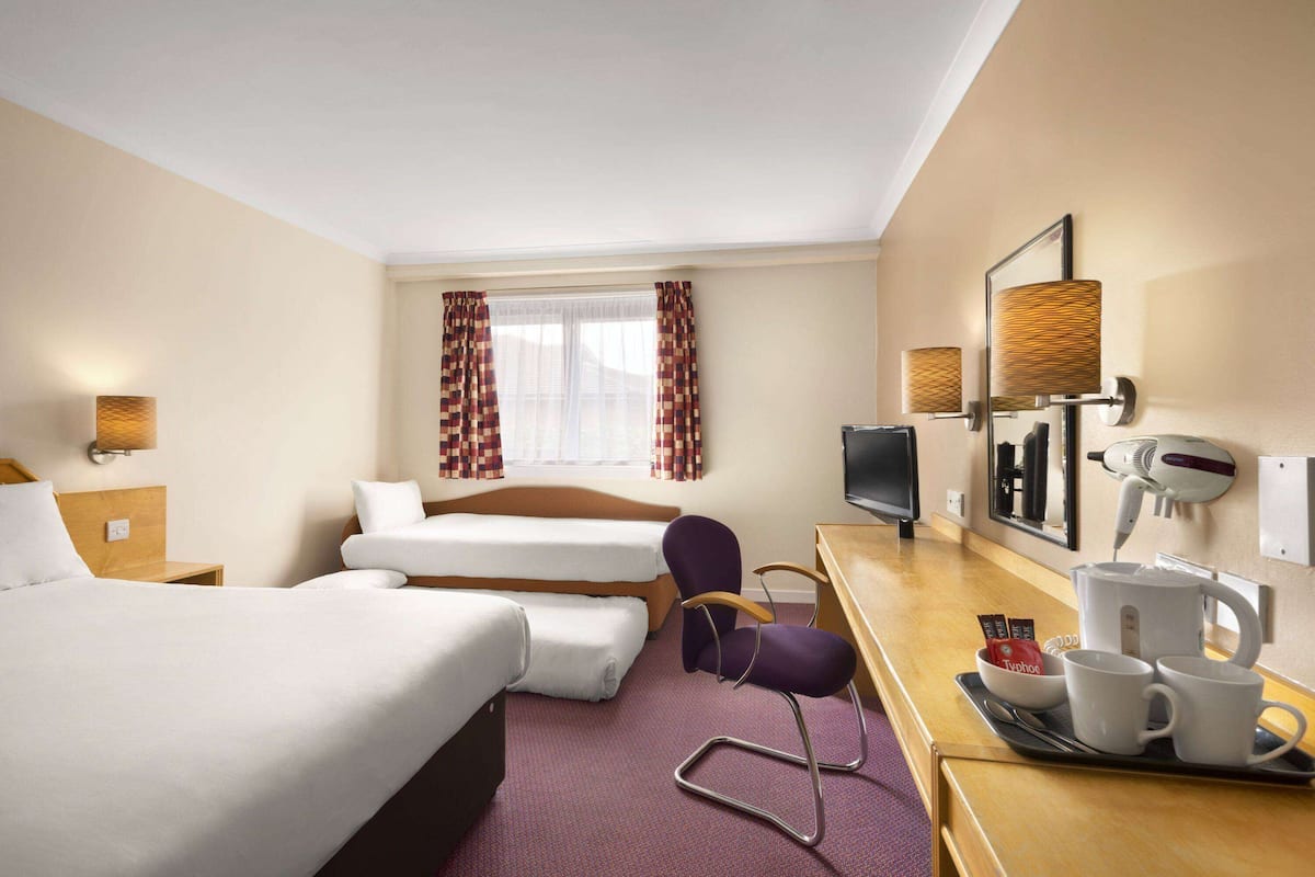 A hotel room with a bed, a desk with a chair, a TV, a hairdryer, and a coffee maker.