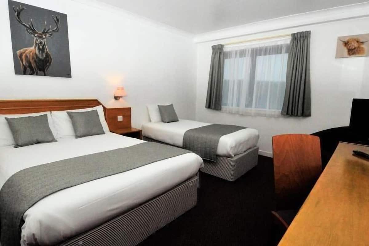 A hotel room with two beds, a desk, a TV, and artwork on the walls.