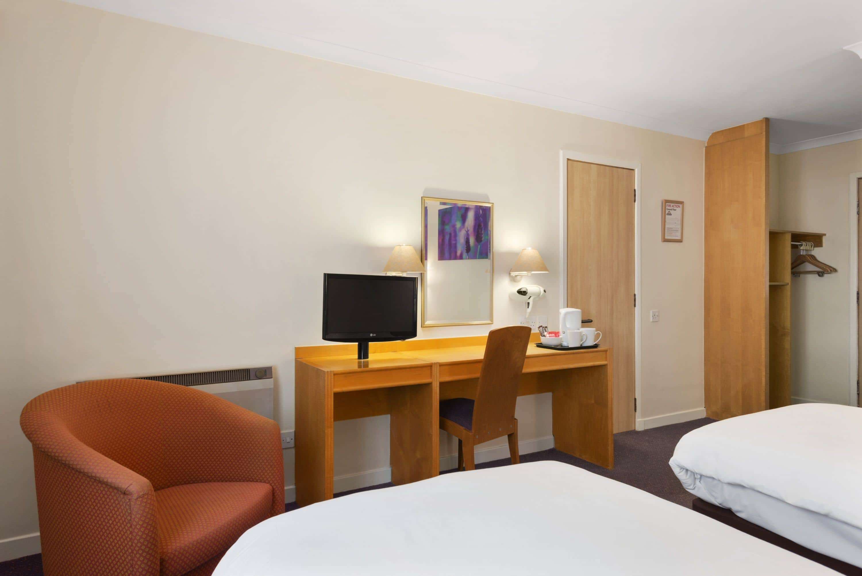 Habitación de hotel con escritorio de madera, una computadora, una silla, una cama y un armario.