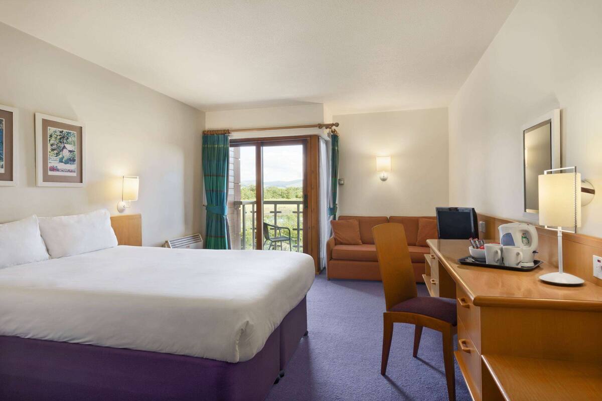 A hotel room with a bed, a desk, a chair, a sofa, and a balcony with a view.