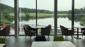 A restaurant with large windows overlooking a lake, wicker chairs, and a view of the surrounding greenery. - Days Inn by Wyndham Lockerbie Annandale Water (Lockerbie)