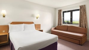 A hotel room with a bed, a nightstand, a lamp, a sofa, and a window with curtains. - Days Inn by Wyndham Lockerbie Annandale Water (Lockerbie)
