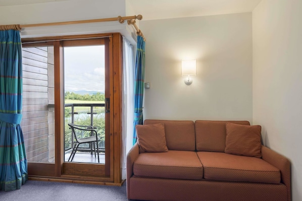 A room with a brown sofa, a sliding glass door leading to an outdoor area with a view, and a wall-mounted light fixture.