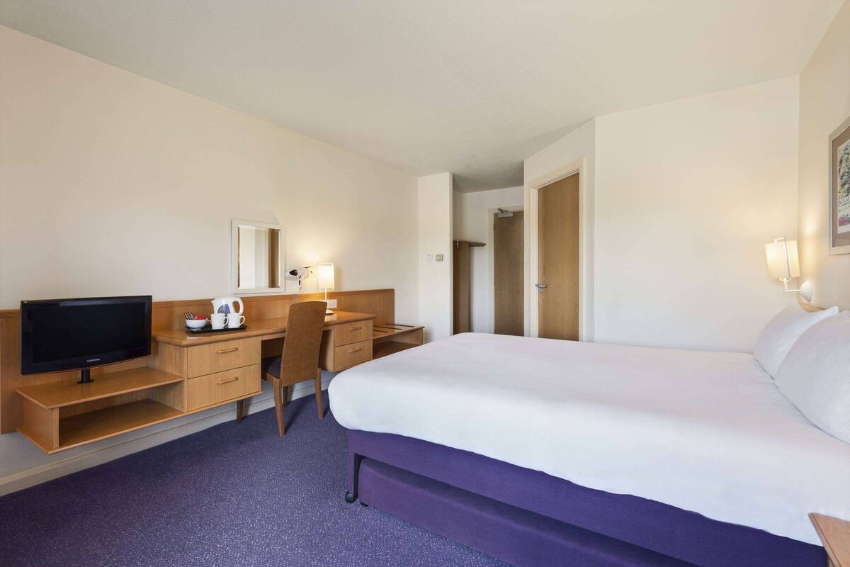 A hotel room with a bed, a desk with a television, a chair, and a wardrobe.