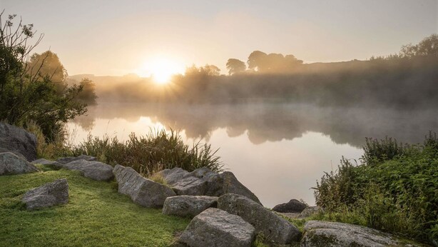 A serene lakeside scene with a clear view of the sunrise, calm water, and surrounding greenery. - Days Inn by Wyndham Lockerbie Annandale Water (Lockerbie)
