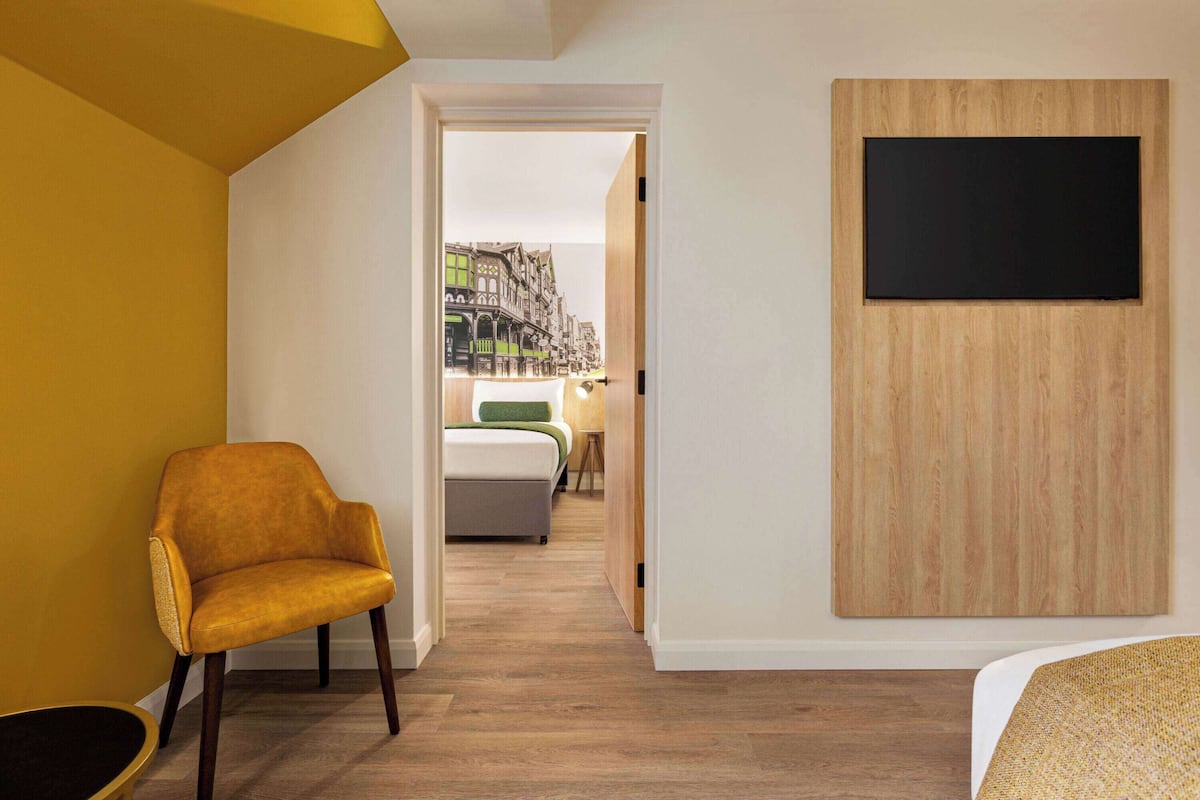 A modern hotel room with a yellow accent wall, a wooden panel wall, and a flat-screen TV mounted on the panel.