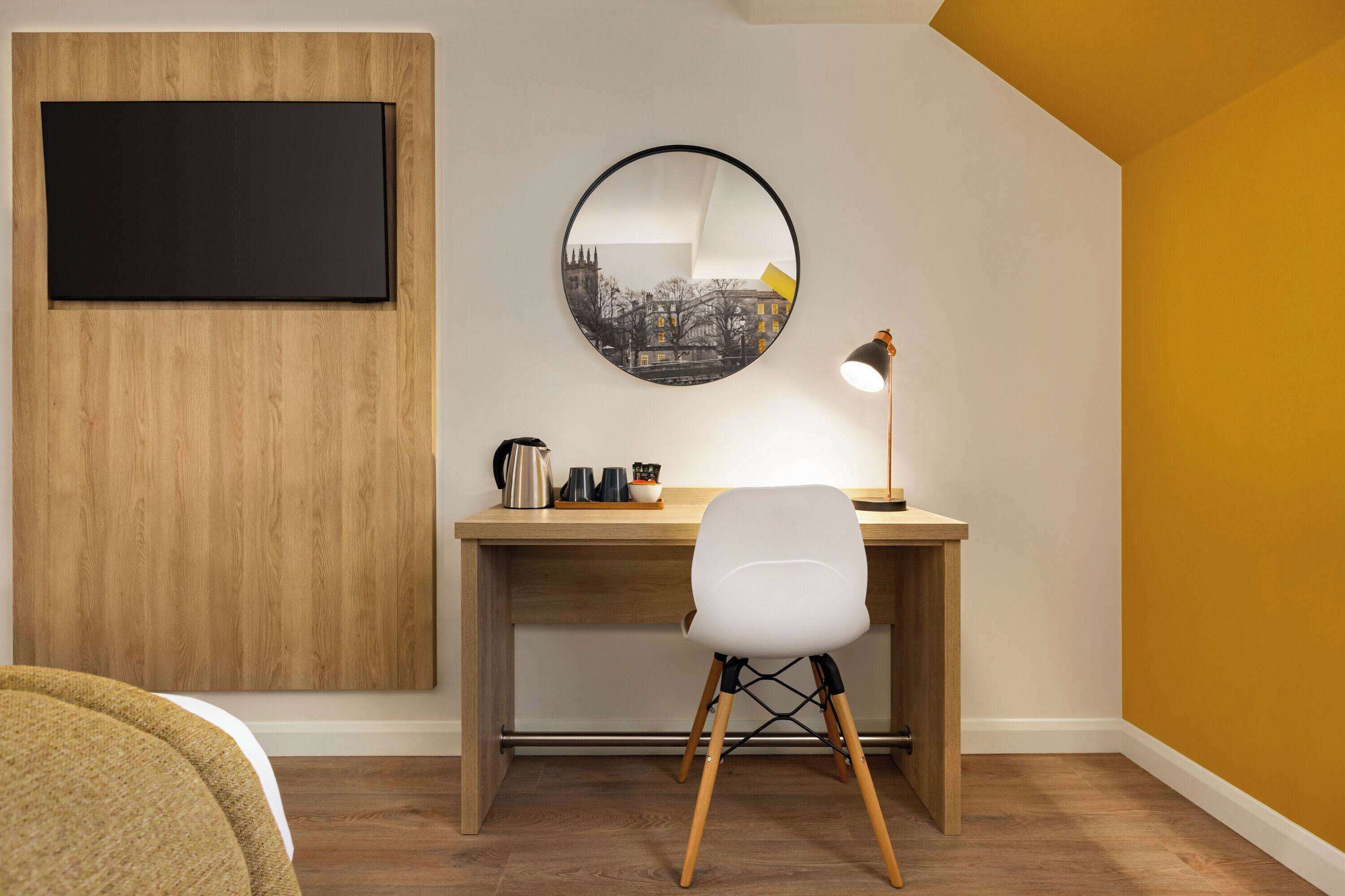 A modern room with a wooden desk, a white chair, a round mirror, and a blackboard.