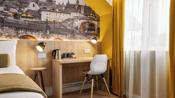 Una habitación de hotel con cama, escritorio y silla, lámpara y un ventanal con cortinas.