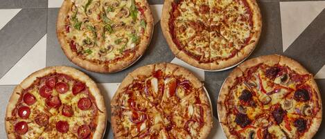 Cinco pizzas con distintos ingredientes dispuestas sobre una mesa.