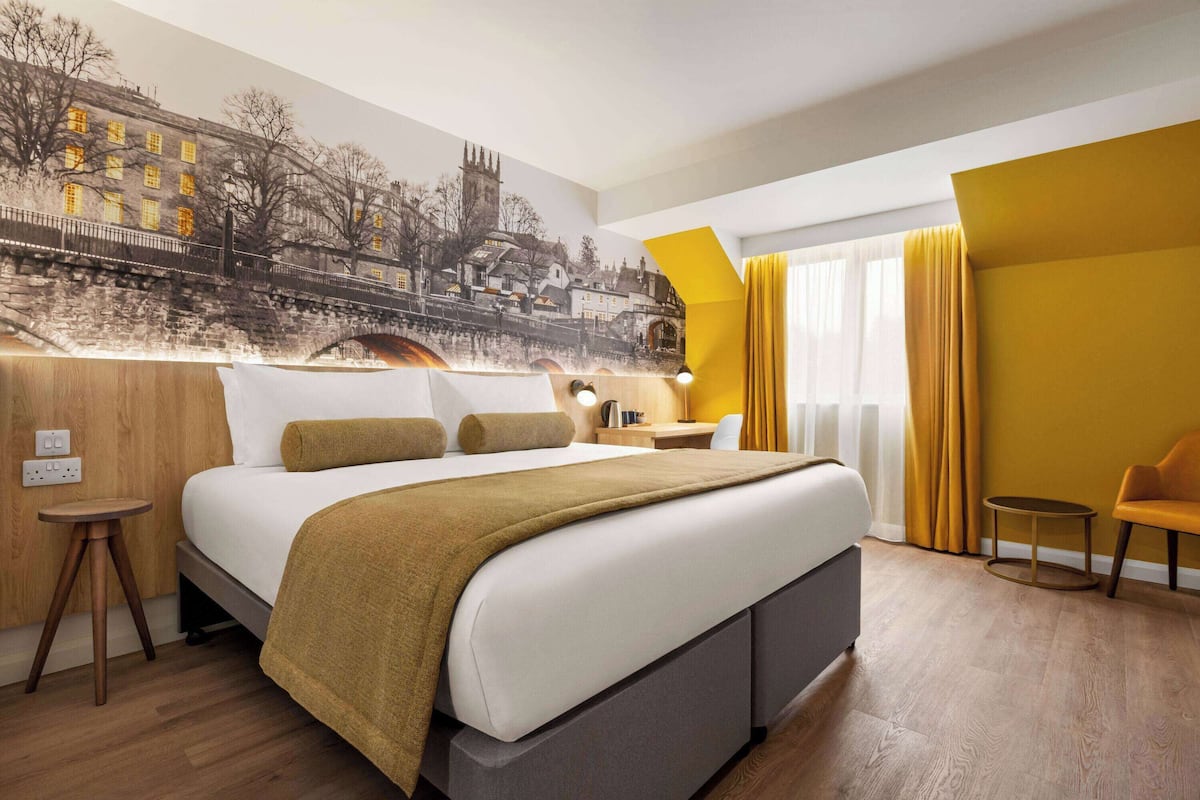A modern hotel room with a large bed, a desk, and a chair.