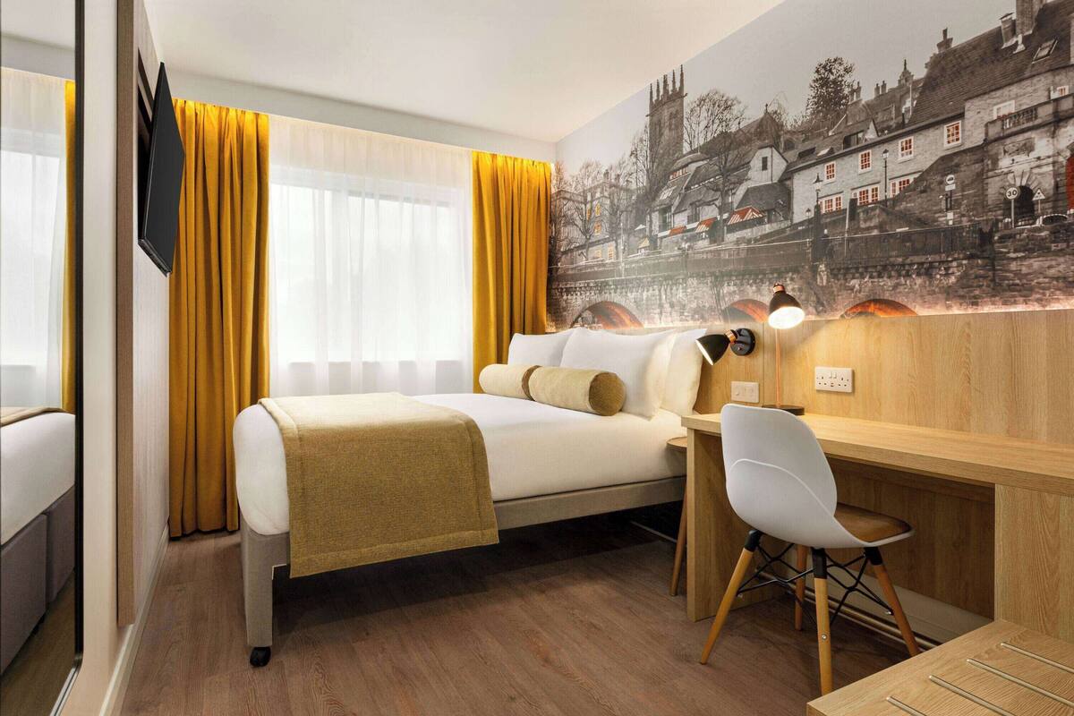 A hotel room with a bed, a desk, a chair, and a large window with curtains.