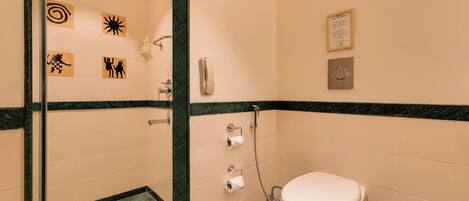 A bathroom with a toilet, a shower, and a hand dryer. There are also toilet paper holders and a hand sanitizer dispenser.