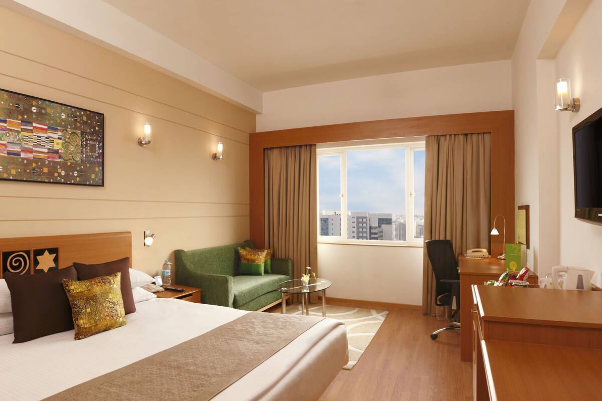 A hotel room with a large bed, a green sofa, a desk, and a TV.