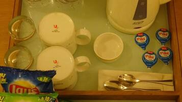 A breakfast tray with a kettle, cups, plates, utensils, and snacks including salted peanuts and lemon tea bags.