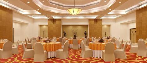 Un salón de banquetes con mesas redondas, sillas blancas y una alfombra roja.