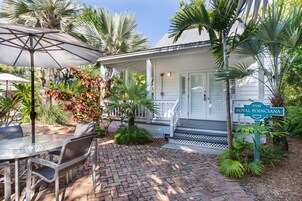 A patio area with a table and chairs, a sign reading "The Royal Poinciana," and a white building with a porch.