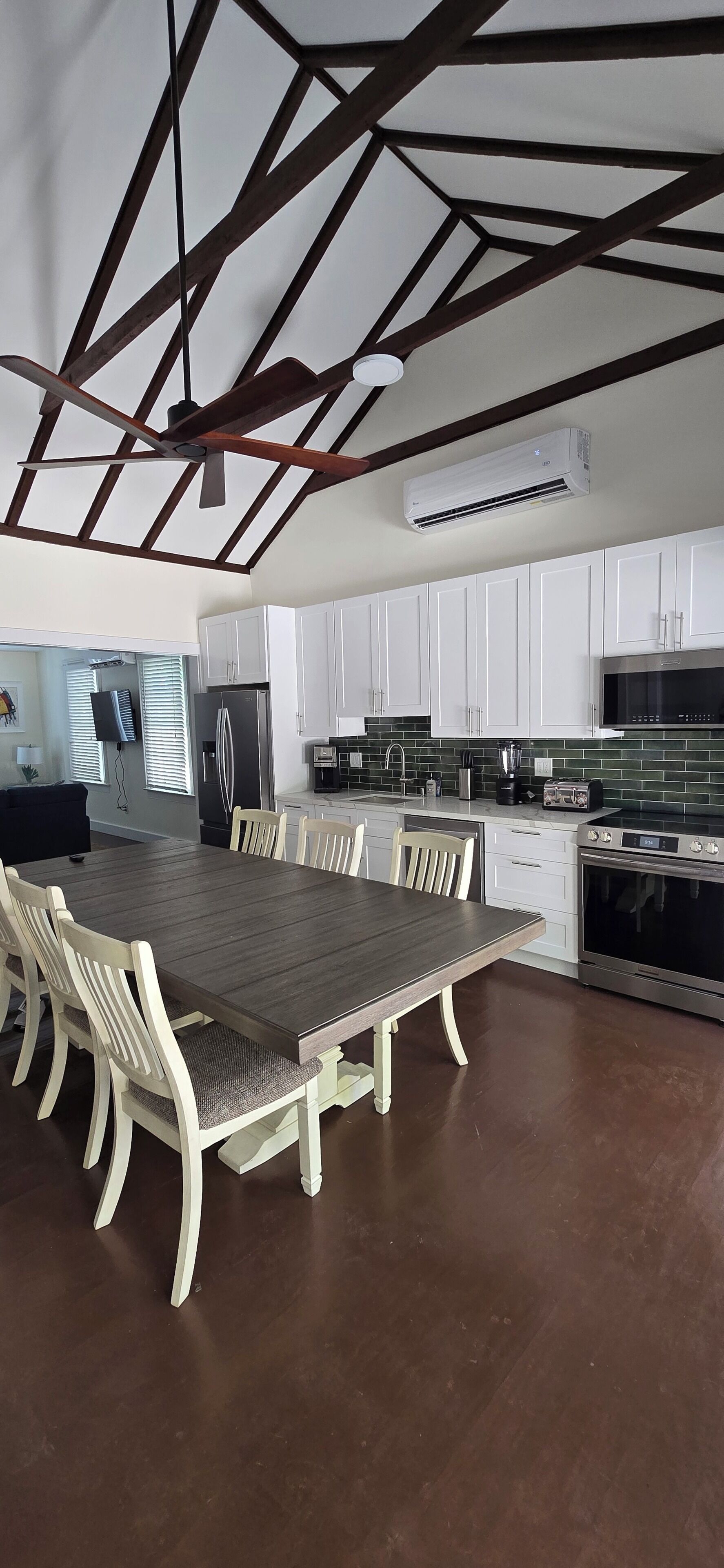 Una cocina moderna con armarios blancos, una mesa de comedor con sillas, un ventilador de techo y un equipo de aire acondicionado.