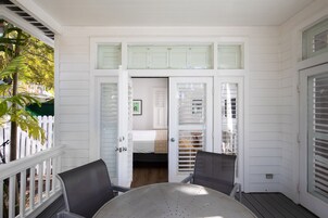 A room with a white exterior, a balcony with a table and chairs, and a bed with a window.