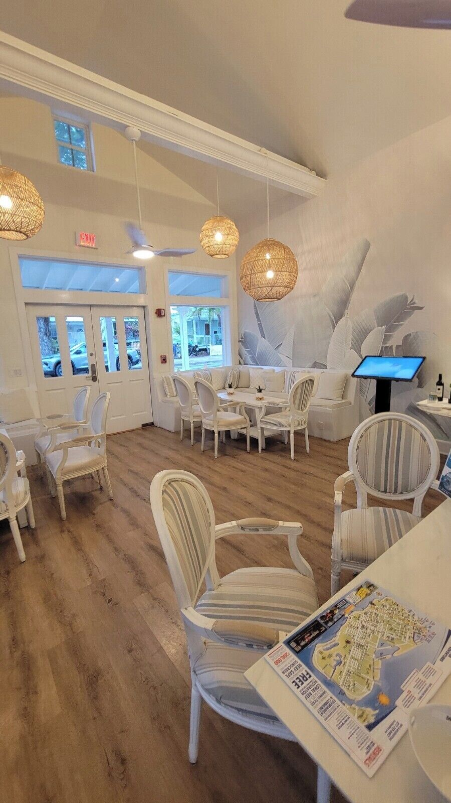 A restaurant with white furniture, wicker ceiling lights, and a view through the windows.