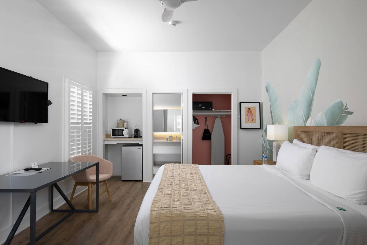 A hotel room with a bed, desk, chair, and a TV.