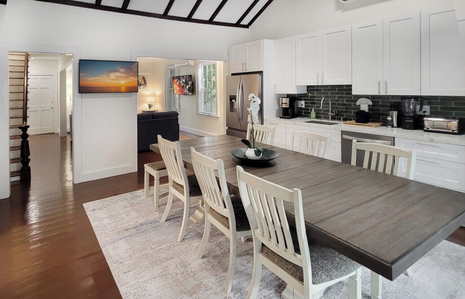 A modern kitchen with white cabinets, a dark wooden dining table, and a view of the living area.