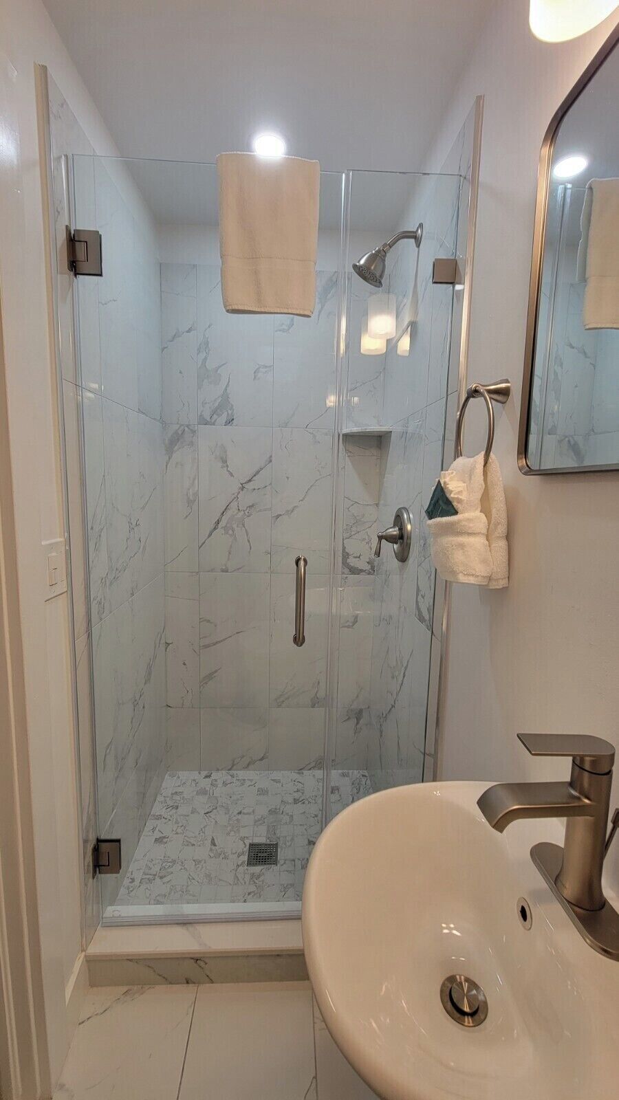 A modern bathroom with a glass-enclosed shower, a white sink, and a mirror.