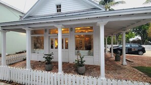 A white building with a covered porch, potted plants, and a white picket fence. - Paradise Inn Key West - Adults Only (Key West)