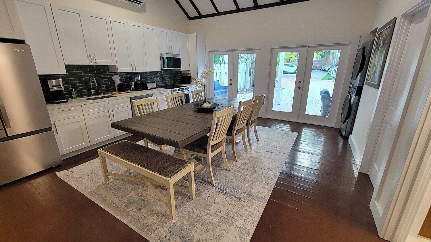 Une cuisine moderne avec des meubles blancs, un plan de travail foncé et un coin repas comprenant une table et des chaises en bois.