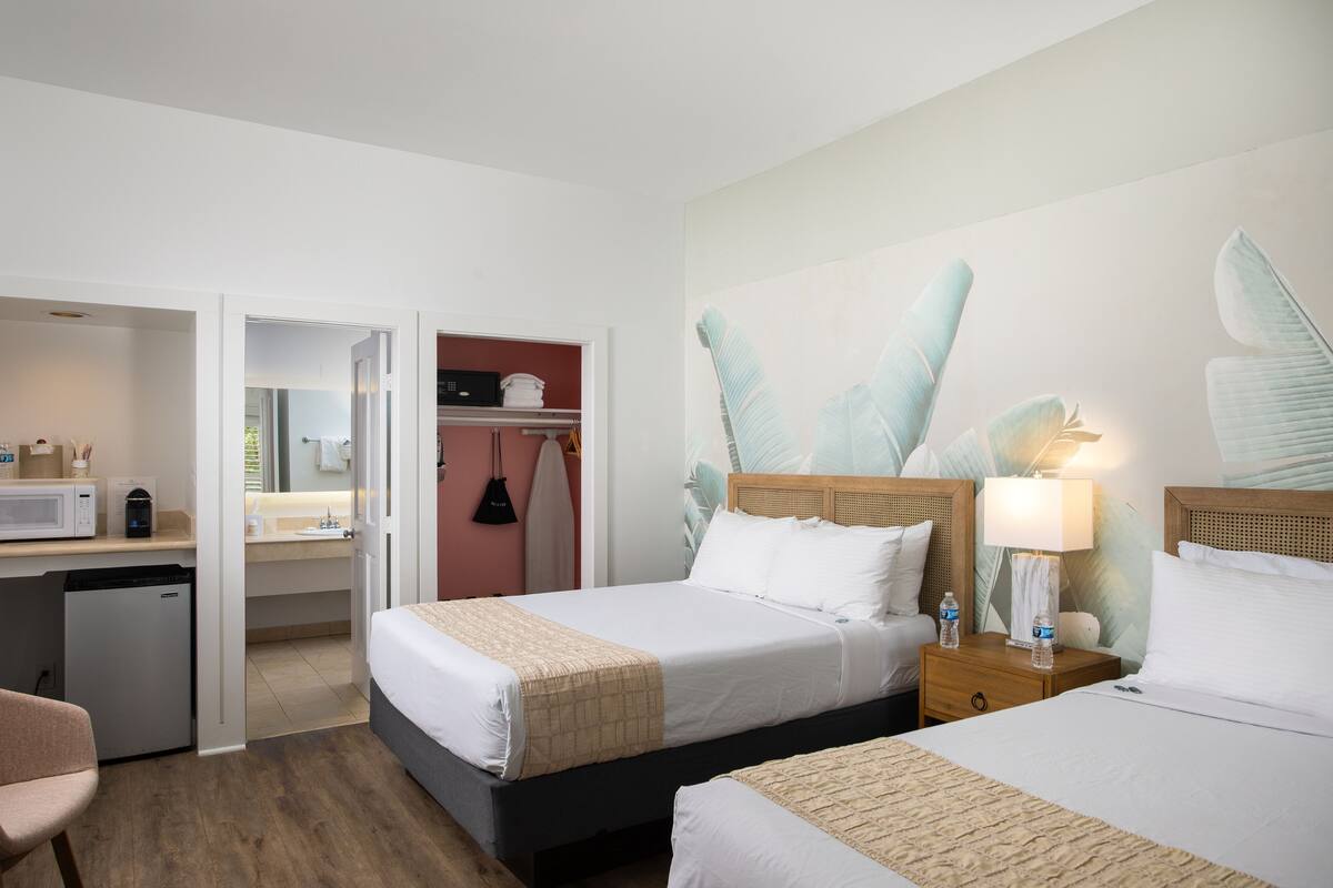 A hotel room with two beds, a desk, a microwave, a mini fridge, and a closet.