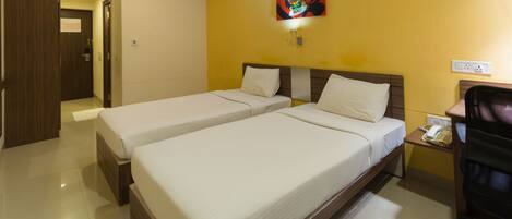 A hotel room with two single beds, a desk with a telephone, a chair, a ceiling fan, and a painting on the wall.