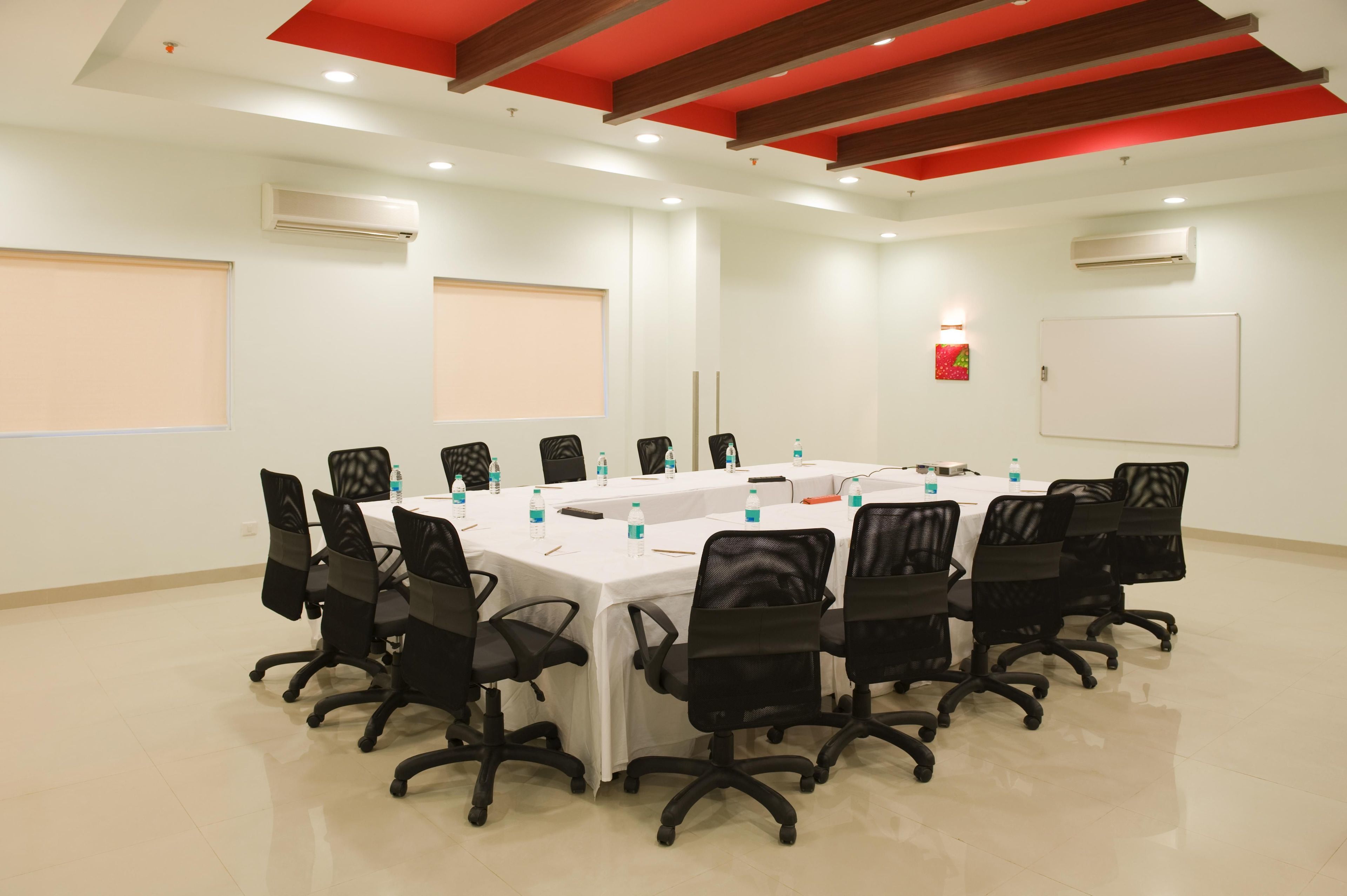 A conference room with a long table, black chairs, white tablecloths, and water bottles.
