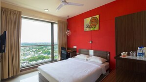 A hotel room with a large bed, a desk, a chair, a TV, and a view of the city through the window. - Ginger Chennai (Chennai)