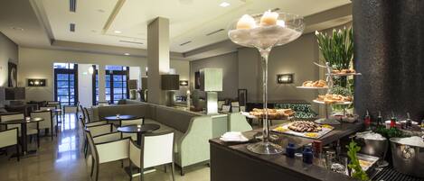 Un moderno vestíbulo de hotel con una zona de bar, diferentes disposiciones de asientos y un bufé con diversas opciones de comida.