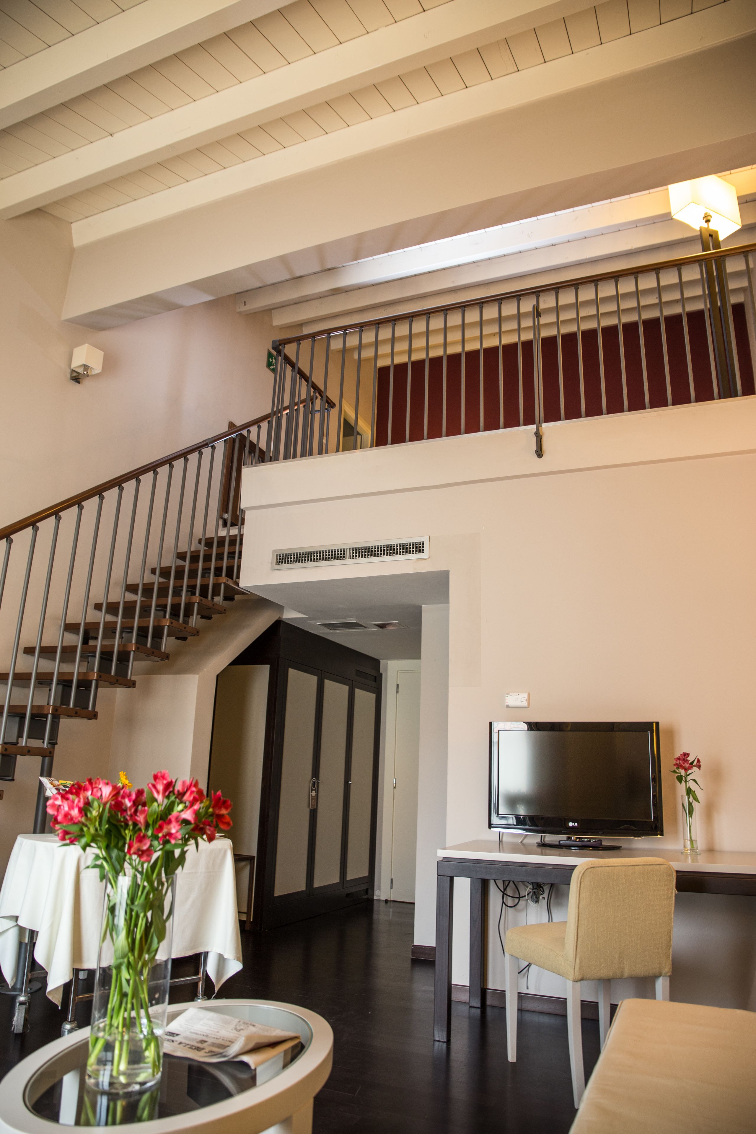 Amplia sala de estar con una escalera, un televisor de pantalla plana, una mesa de comedor y un jarrón con flores.