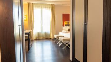 A hotel room with a bed, two bedside tables, a chair, a desk, and a large window with curtains.
