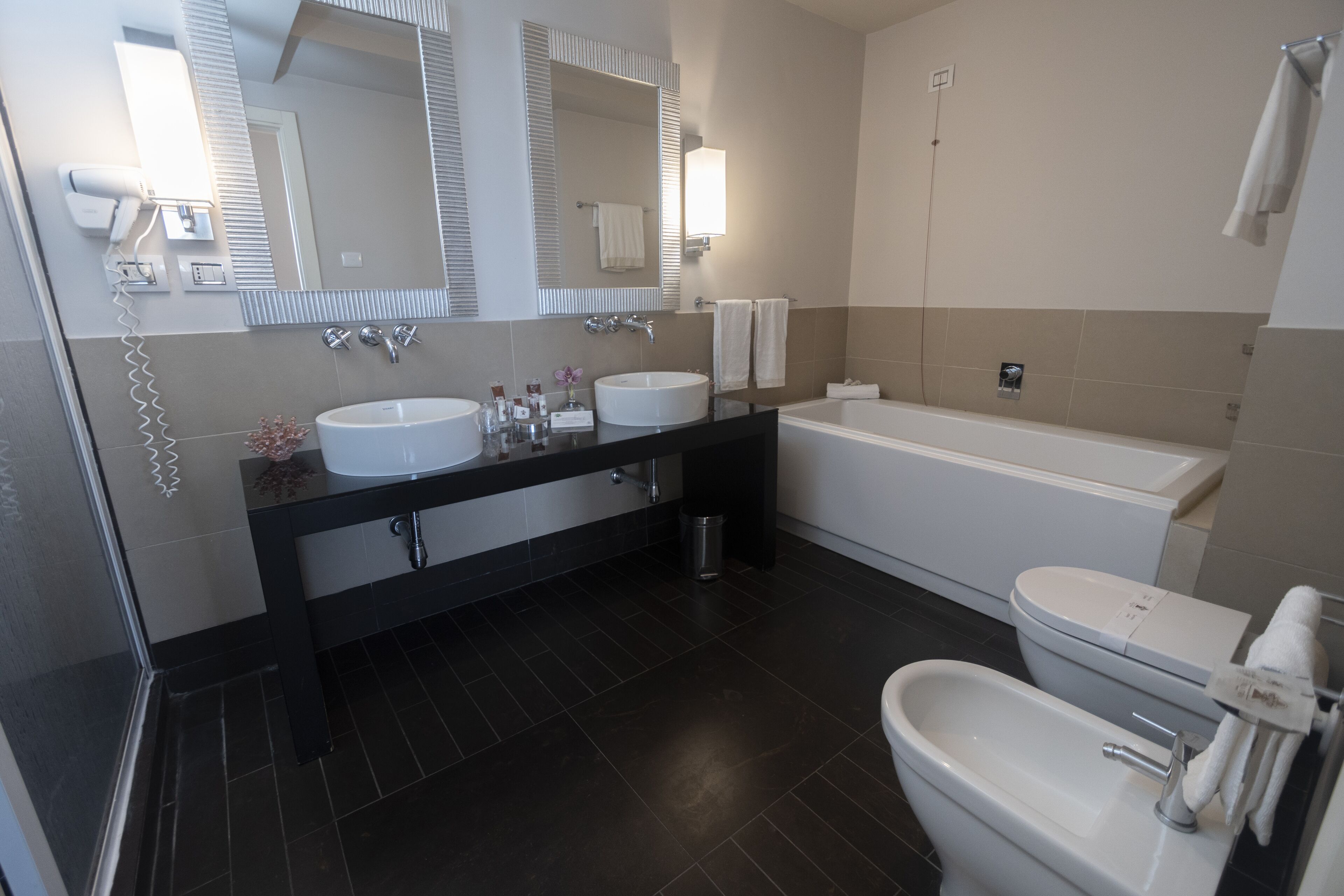 A modern bathroom with two sinks, a bathtub, and a bidet.