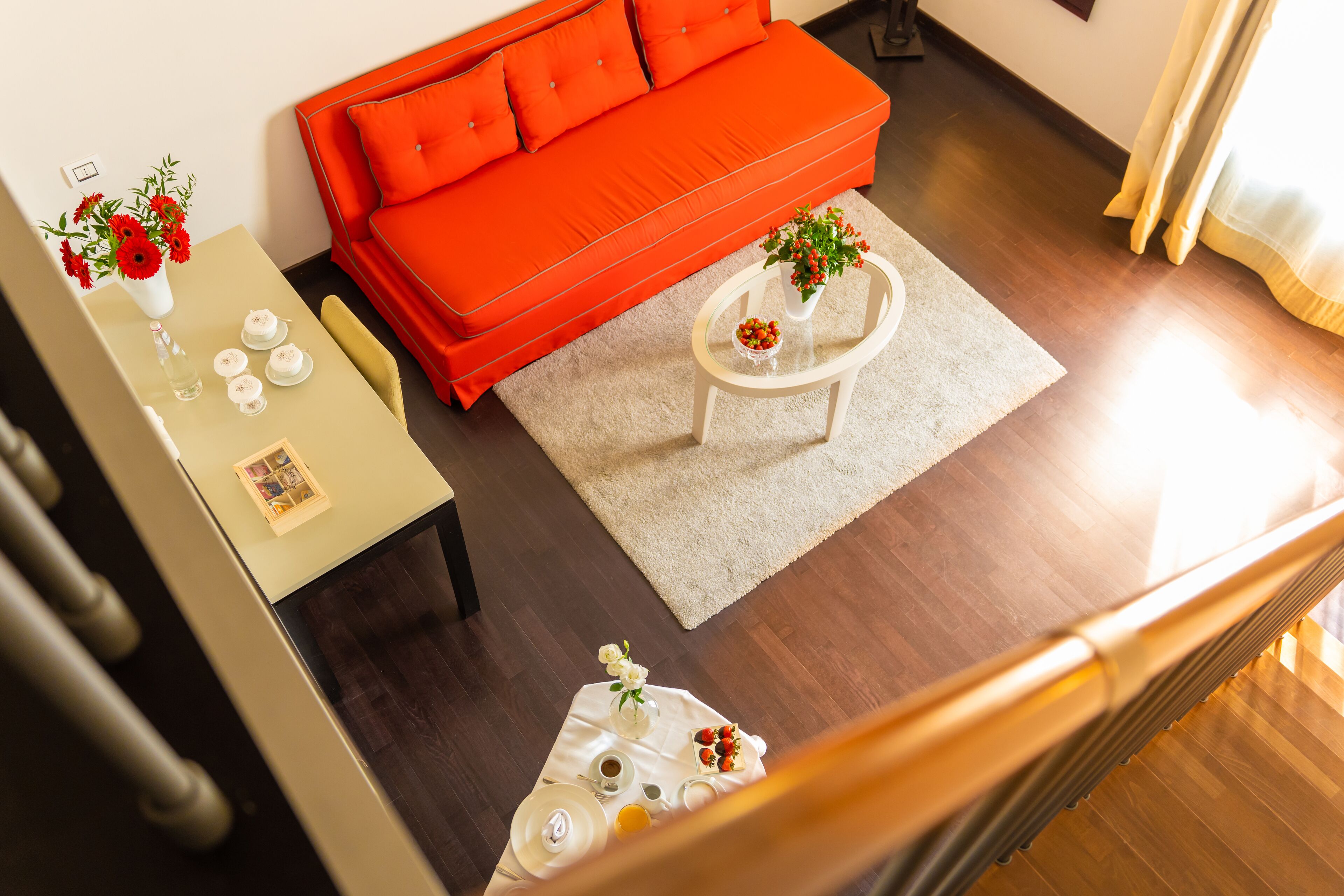 Un salon moderne avec un canapé rouge, une table basse et une table à manger agrémentée d’un vase de fleurs.