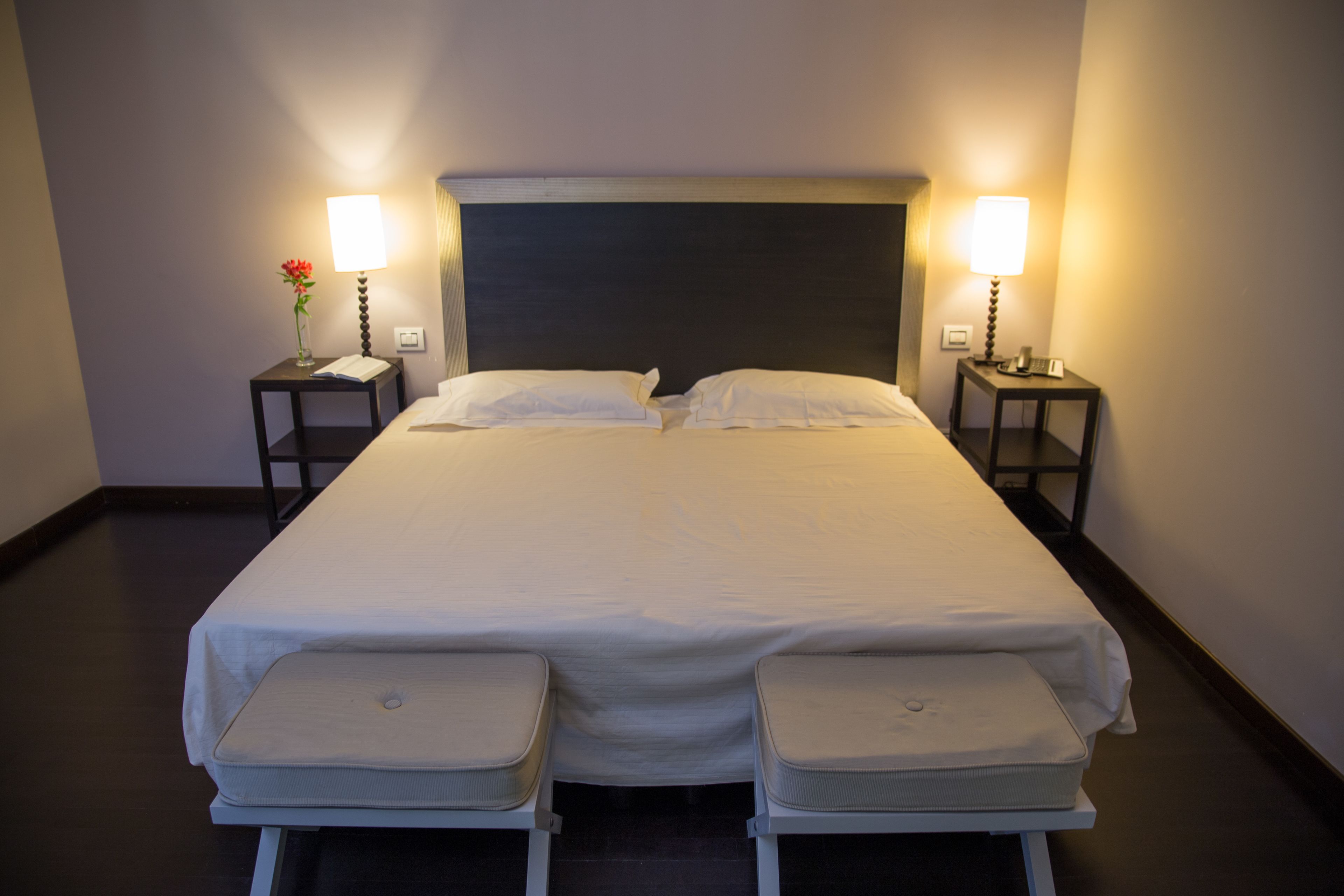 A neatly made double bed with two bedside tables, each with a lamp and a small vase.