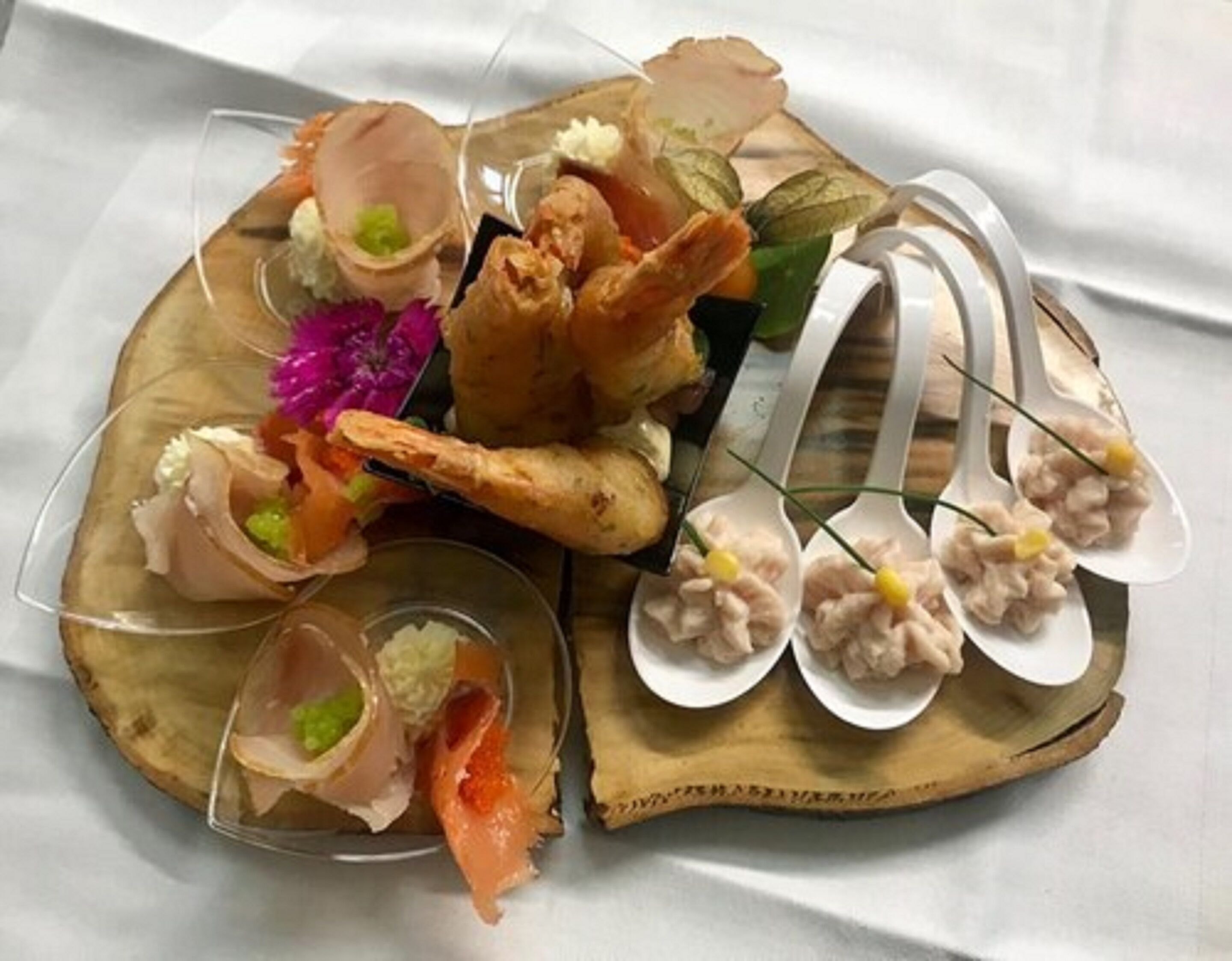 A wooden serving board with various seafood dishes, including shrimp, crab, and possibly sushi, arranged on a white tablecloth.