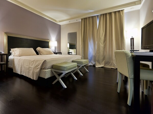 A hotel room with a large bed, a desk with a chair, a television, and a window with curtains. - Grand Hotel Villa Itria (Viagrande)