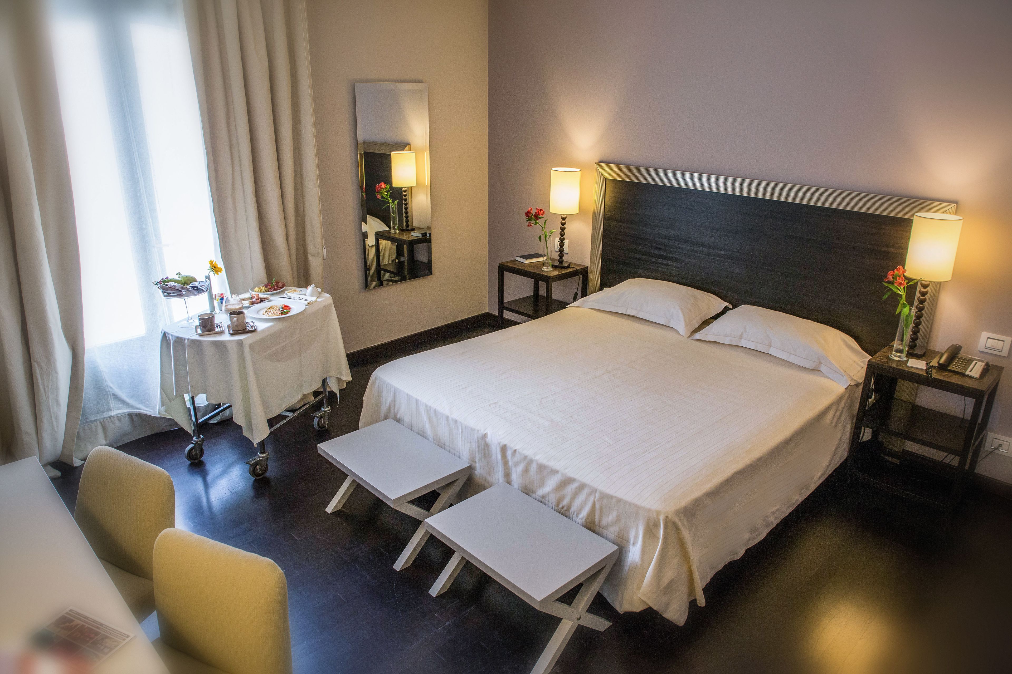 Een hotelkamer met een groot bed, nachtkastjes met lampen, een klein tafeltje met ontbijtartikelen en een stoel.