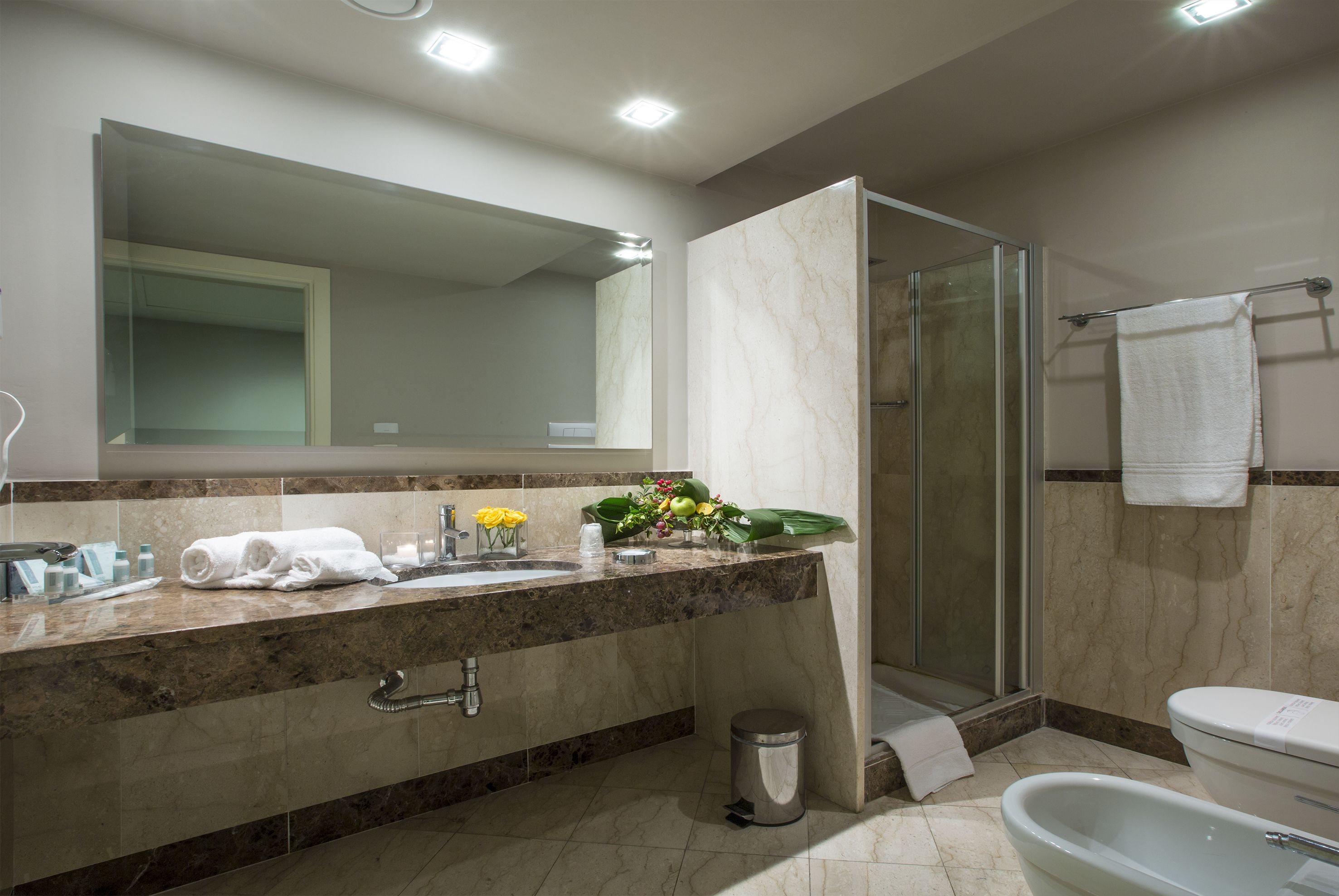 Un baño moderno con encimera de mármol, ducha con cerramiento de vidrio y inodoro blanco.