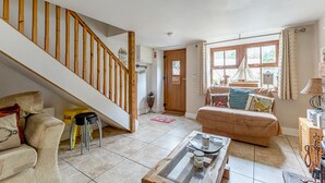 A spacious living area with a wooden staircase, a sofa, a coffee table, and a window with a view of greenery. - Priest Bridge Cottage (Newcastle)